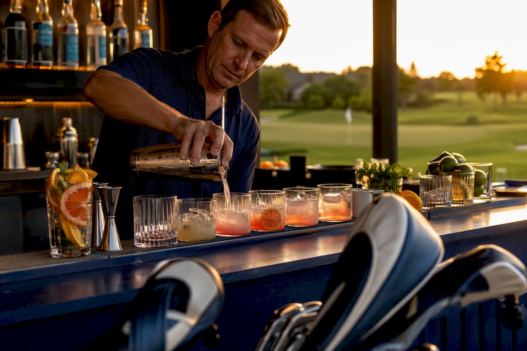 Bartender pouring multiple vodka drinks at golf event bar
