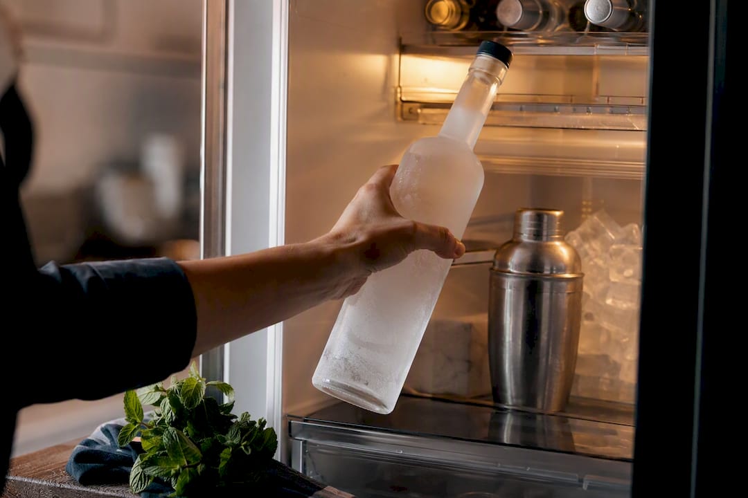 Hand placing vodka bottle in freezer